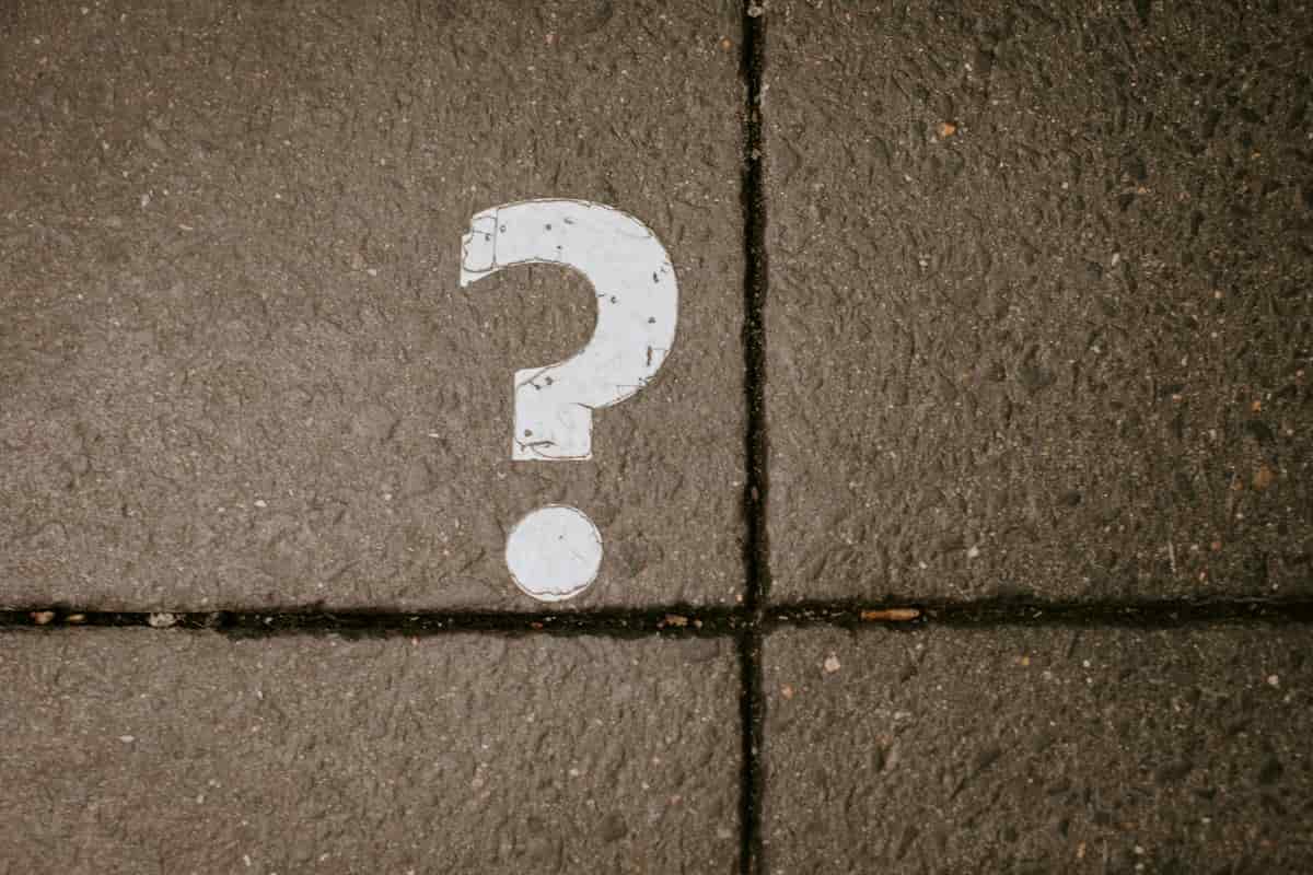 A white question mark painted on a dark paved sidewalk, split by two grout lines.