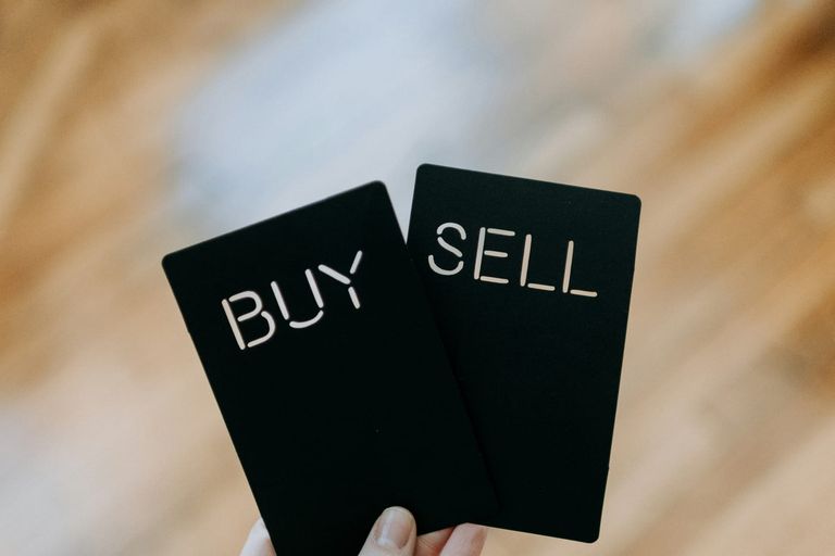 A hand holding two black cards with the words Buy and Sell cut out of them.