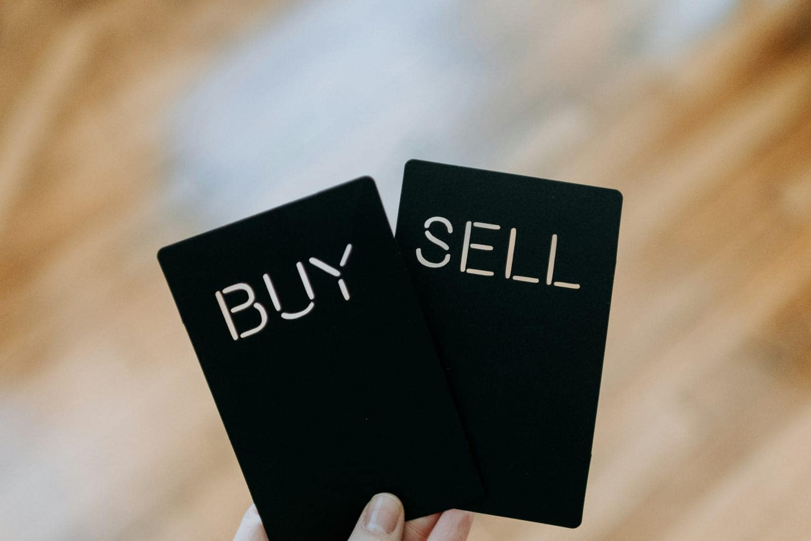 A hand holding two black cards with the words Buy and Sell cut out of them.
