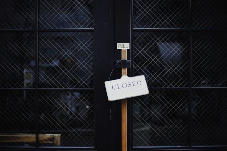 A white sign reading Closed hanging from the wooden handle of a black wire-glass door.
