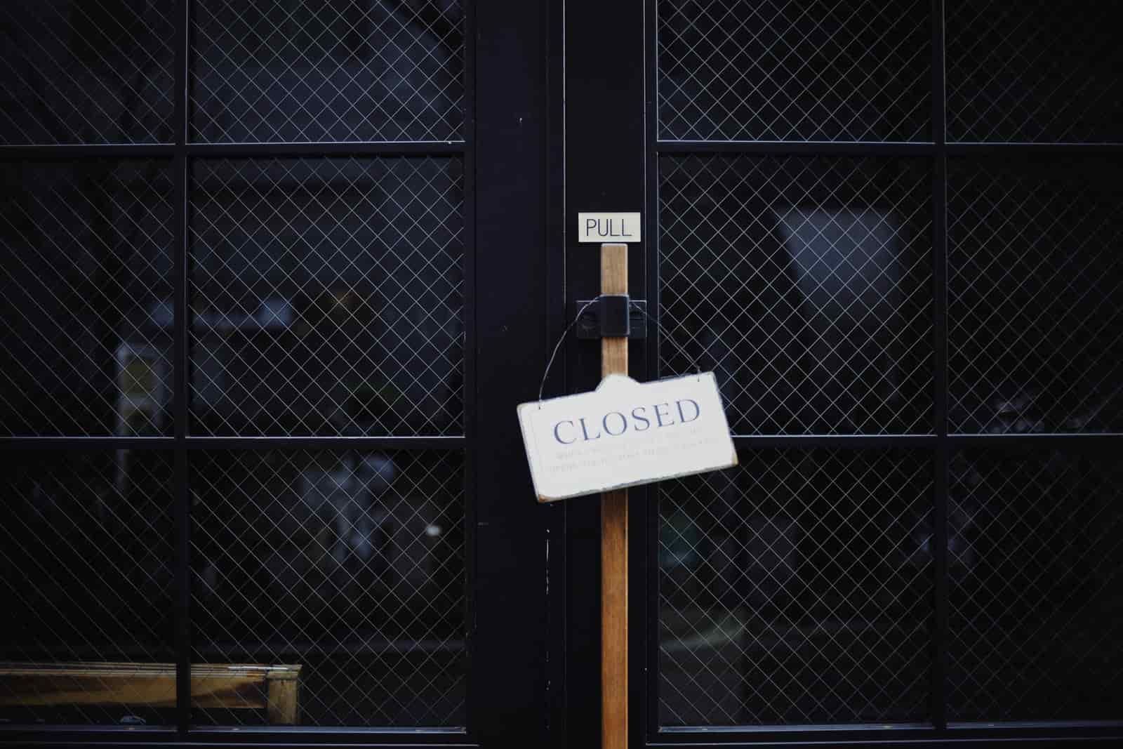 A white sign reading Closed hanging from the wooden handle of a black wire-glass door.