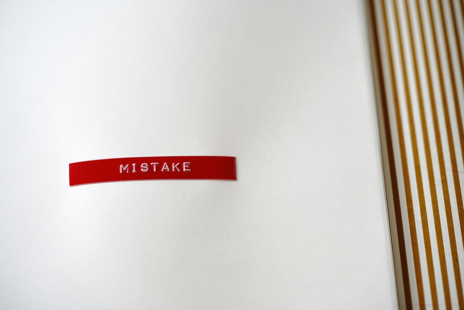 A red label embossed with the word MISTAKE on a blank notebook page.