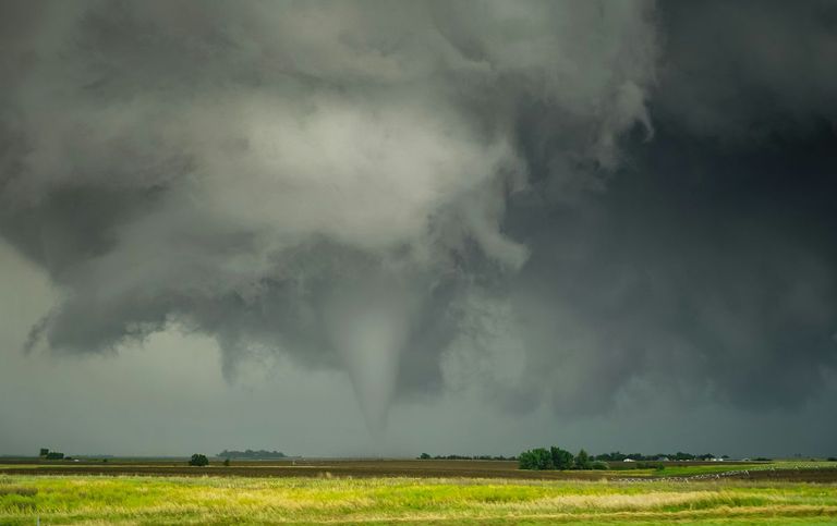 A tornado funnel descending from a dark storm cloud over green farmland.