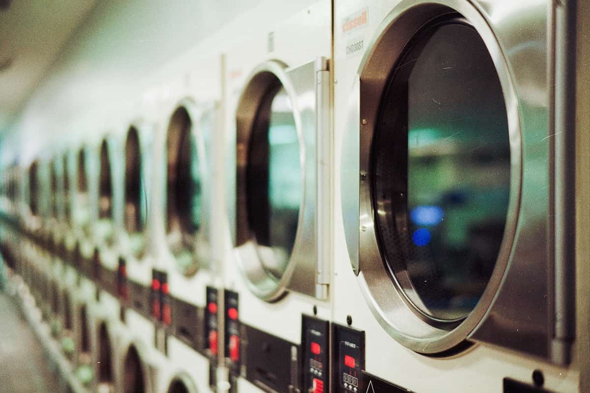 A long row of stainless steel laundromat dryers with round glass doors, fading out of focus.